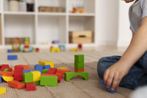 Foto de alumno sentado en el suelo jugando con piezas de madera de colores